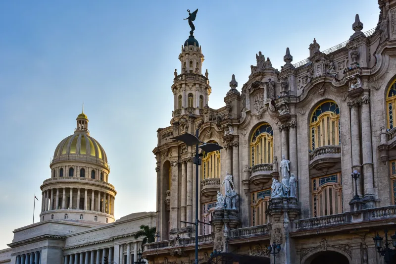 View of the National Capitol Building and Grand Theater in Havana, Cuba against a blue sky.