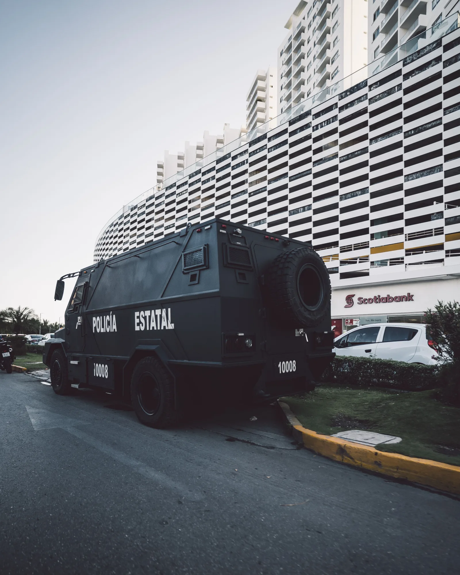 Escena callejera urbana con un vehículo policial cerca de un edificio moderno de gran altura durante el día.