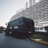 Escena callejera urbana con un vehículo policial cerca de un edificio moderno de gran altura durante el día.