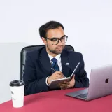Empresario profesional tomando notas en un escritorio con una laptop y café. Ideal para temáticas de oficina.