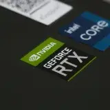 Primer plano de los stickers NVIDIA GeForce RTX e Intel Core i7 en la superficie de una laptop, mostrando tecnología moderna.