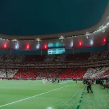 Un estadio de fútbol por la noche con coloridas exhibiciones de la afición y una atmósfera enérgica.