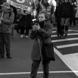 An elderly woman captures a street protest with her mobile phone, black and white image.