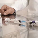 Un veterinario en un entorno clínico prepara jeringas y frascos de vacuna sobre una superficie reflectante.