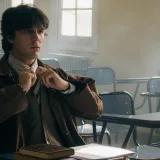 A student in a foggy, empty classroom adjusts his tie, reflecting a thoughtful mood.