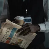 Primer plano de un periodista sosteniendo un periódico y una taza de café, transmitiendo el concepto de prensa y medios.
