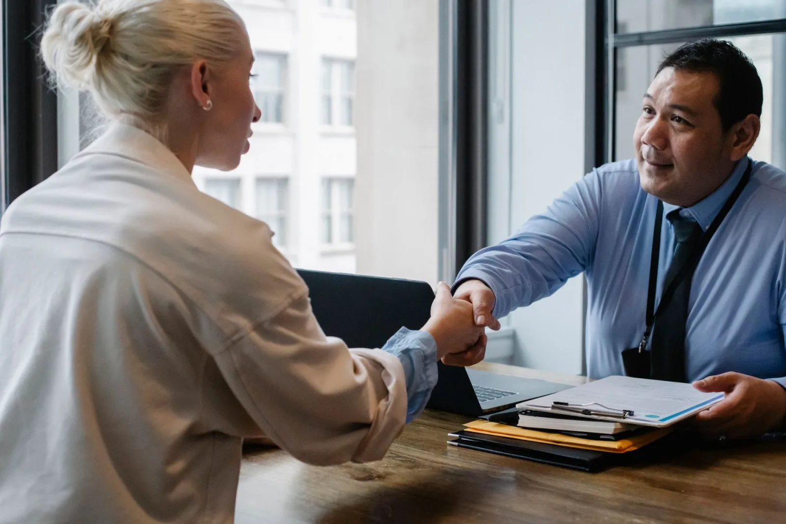 Emprendedor de una minoría étnica estrechando la mano de una candidata durante una entrevista de trabajo en una empresa.