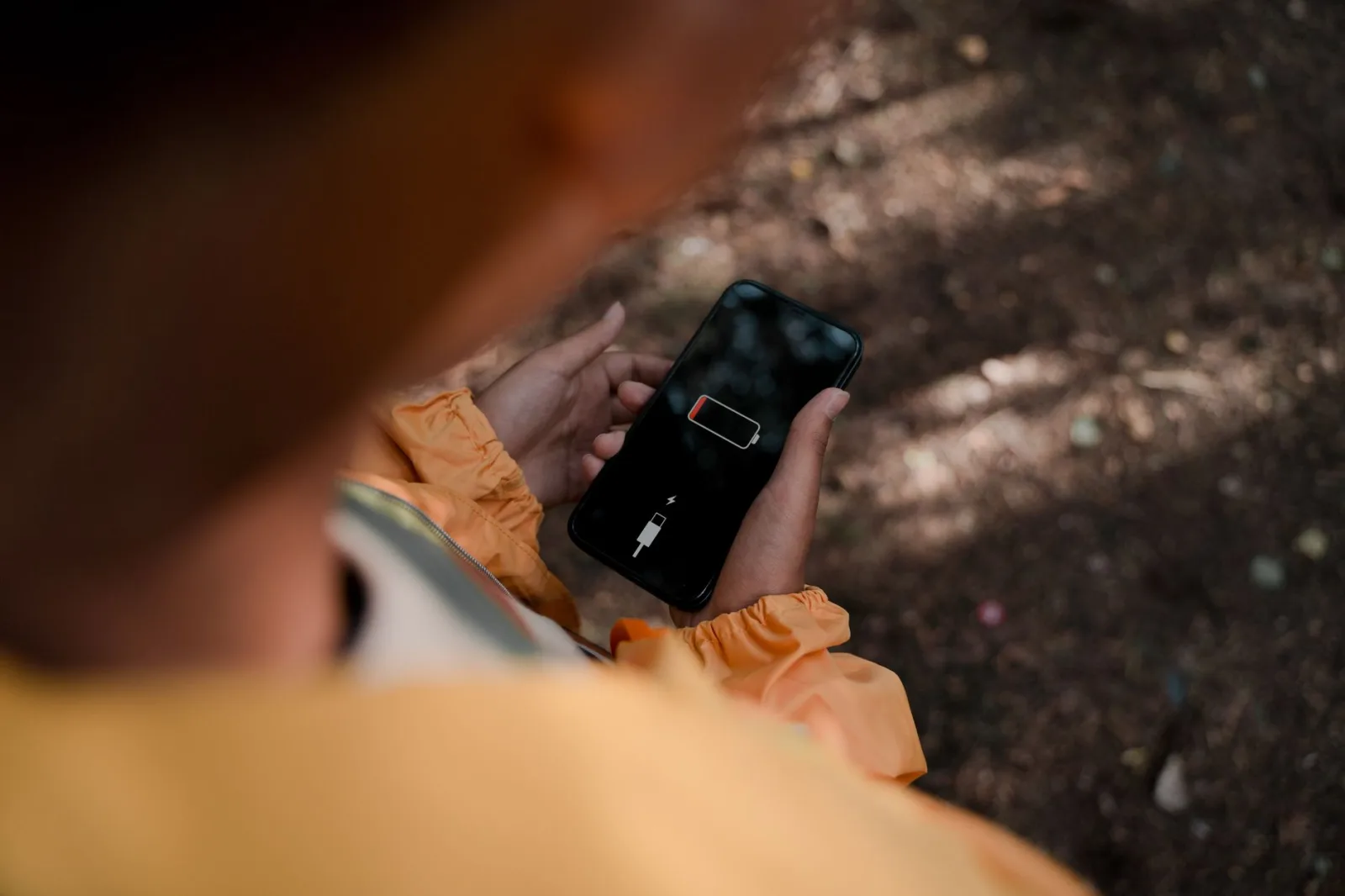 Un adolescente sostiene un teléfono inteligente que muestra poca batería al aire libre, en un bosque.