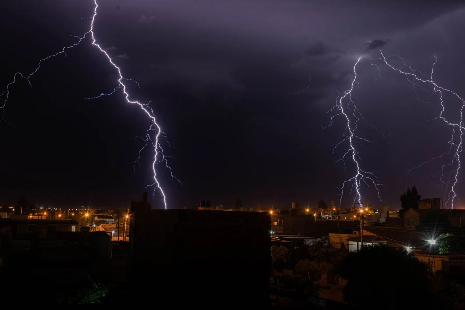 Un intenso relámpago ilumina una ciudad durante una tormenta eléctrica nocturna, mostrando el poder de la naturaleza.