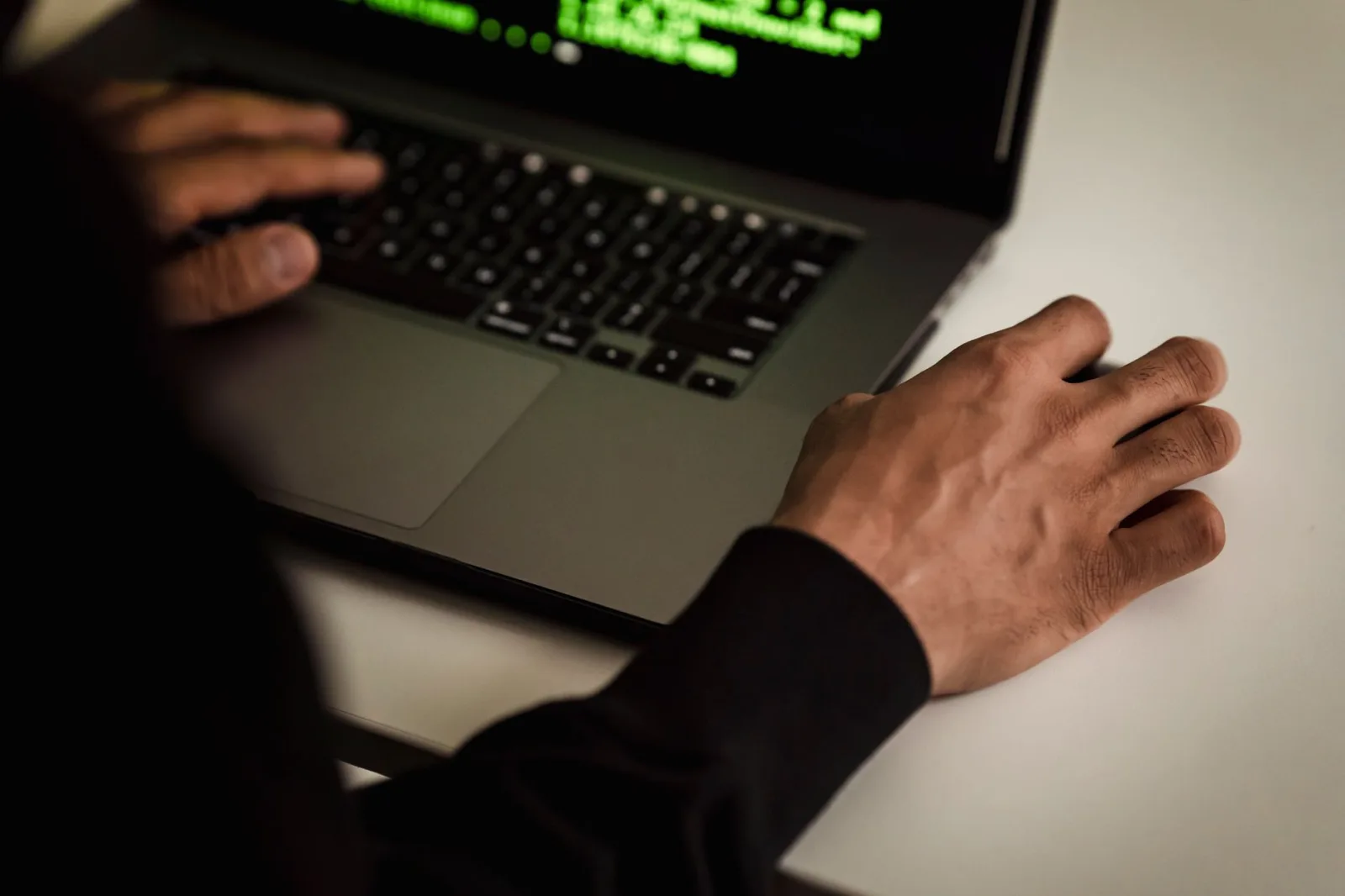 Vista desde arriba de un desarrollador sin rostro, vestido con una sudadera negra con capucha, que escribe código en una netbook mientras trabaja en un estudio luminoso.