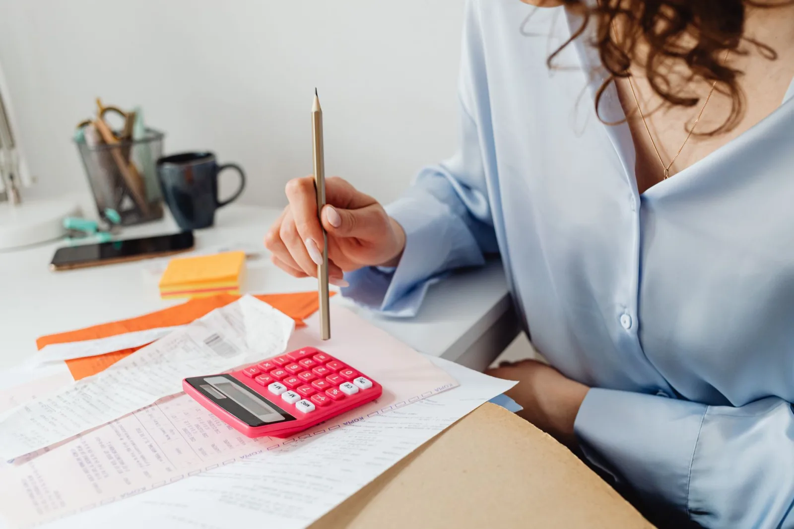 Una mujer calcula gastos con una calculadora y unos papeles en su escritorio.