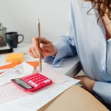 Una mujer calcula gastos con una calculadora y unos papeles en su escritorio.