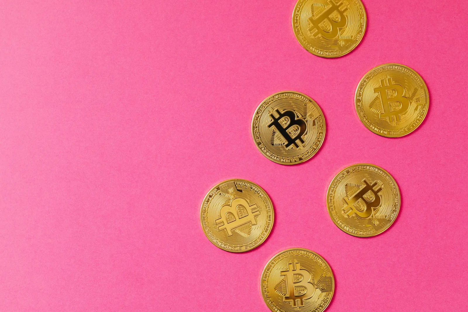 Monedas doradas de Bitcoin sobre una superficie rosa vibrante, que representan la inversión en criptomonedas y blockchain.