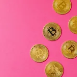 Monedas doradas de Bitcoin sobre una superficie rosa vibrante, que representan la inversión en criptomonedas y blockchain.