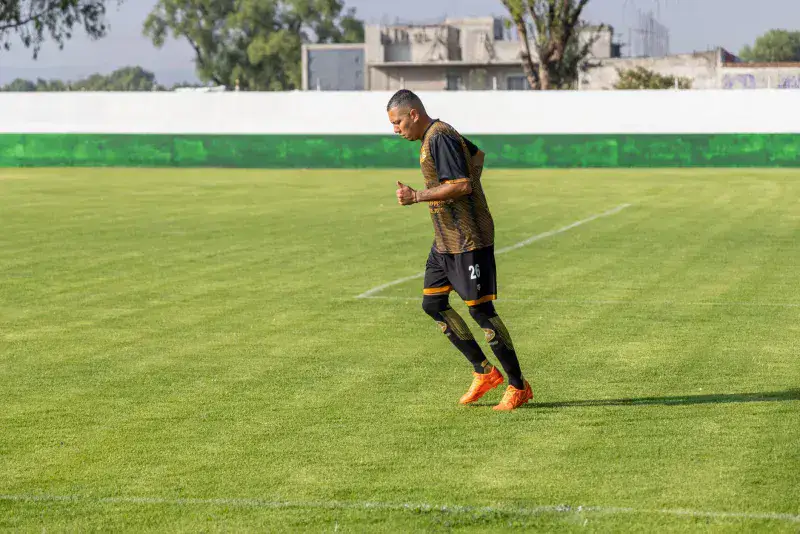 An adult male soccer player jogging on a grassy field during daytime training.
