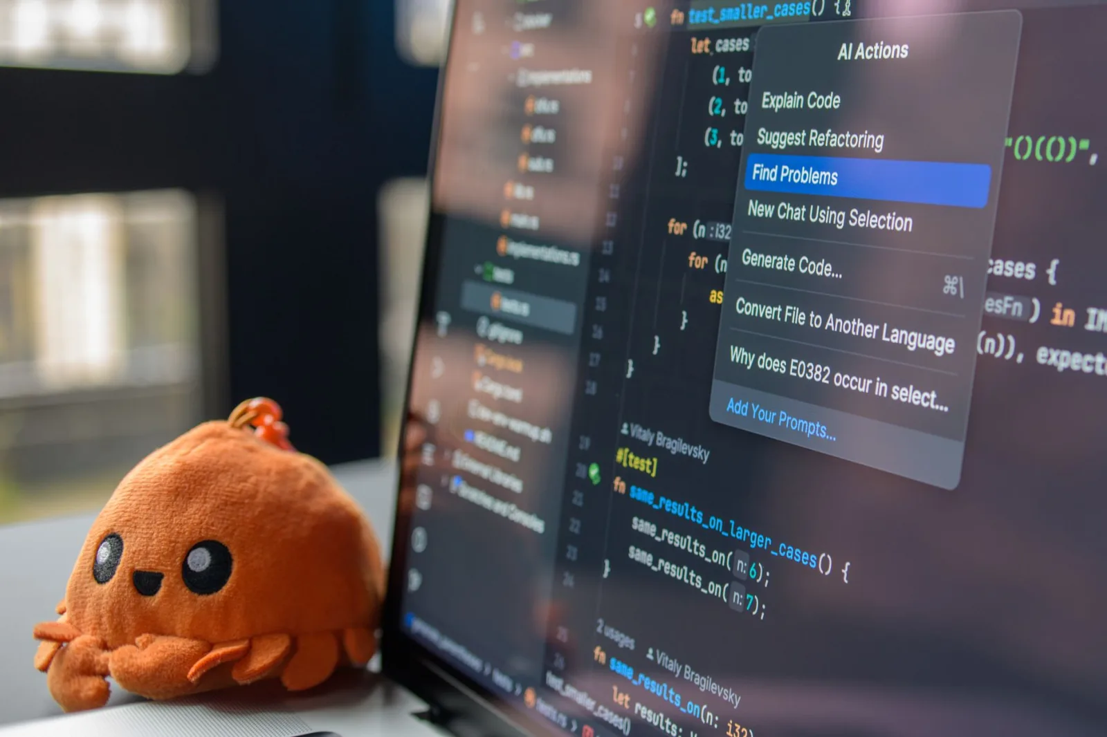 La pantalla de una computadora portátil muestra un editor de código con un adorable peluche de cangrejo naranja a su lado.