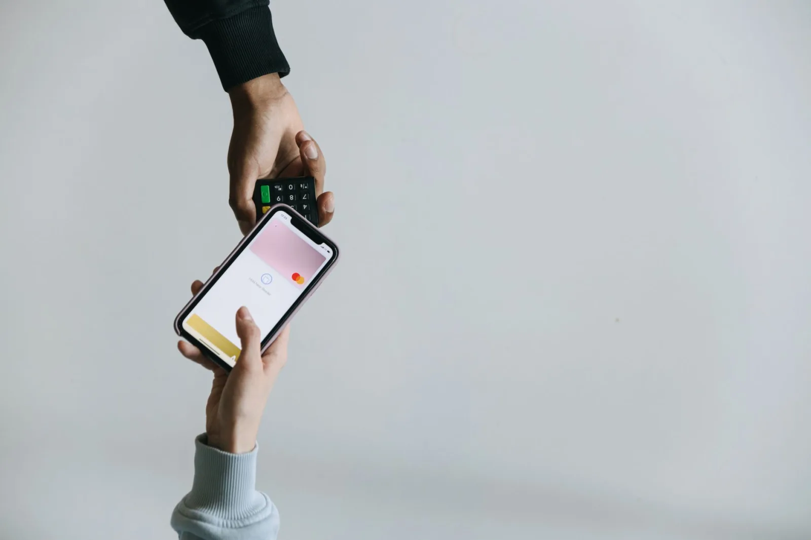 Manos usando un teléfono inteligente y una terminal para realizar un pago sin efectivo, mostrando métodos de transacción modernos.