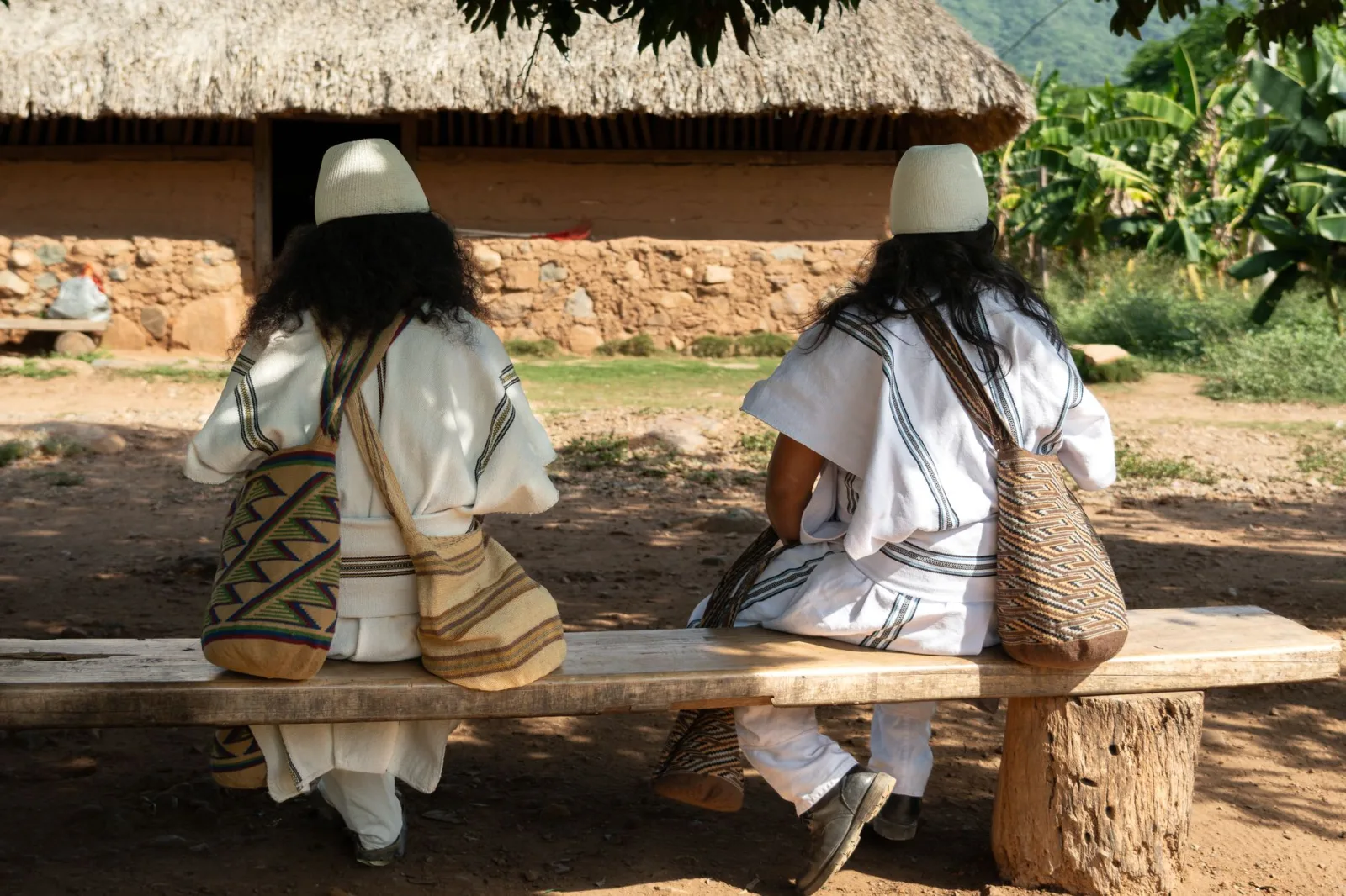 Vista desde atrás de dos personas indígenas con vestimenta tradicional en Pueblo Bello, Colombia.