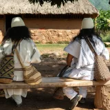 Vista desde atrás de dos personas indígenas con vestimenta tradicional en Pueblo Bello, Colombia.