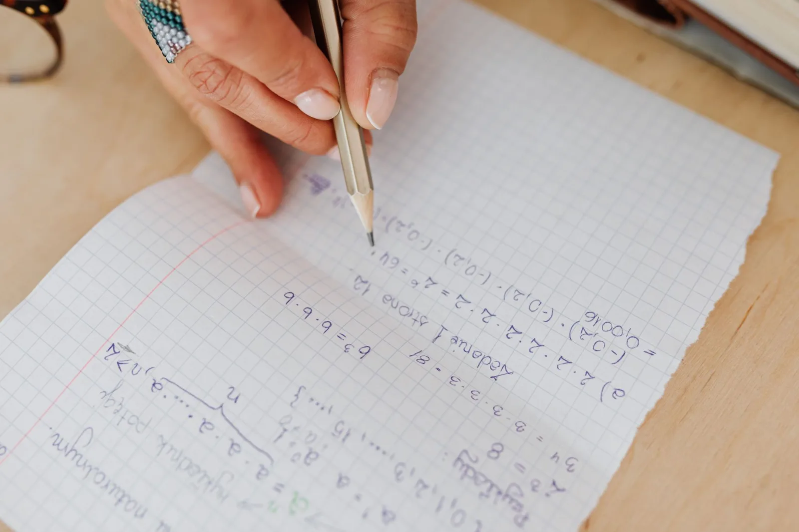 Una persona escribe ecuaciones matemáticas a mano con un lápiz sobre papel cuadriculado, lo que fomenta el aprendizaje.