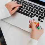 Primer plano de una persona usando una computadora portátil y sosteniendo una tarjeta de crédito para hacer compras en línea.