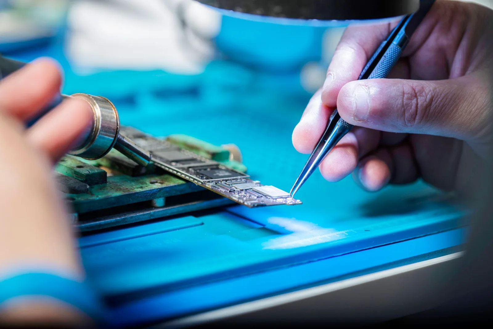 Manos sujetan con delicadeza herramientas para reparar una placa de circuito con precisión.