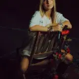 Young woman seated on chair with microphone and rose decorations outdoors during the night.