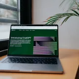 Una laptop que muestra ChatGPT sobre un escritorio junto a una ventana, en un moderno espacio de trabajo en casa.