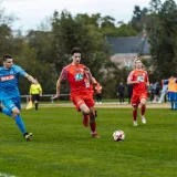 Acción dinámica de un partido de fútbol capturada en Francia con jugadores con camisetas rojas y azules.