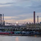 A large industrial refinery complex next to a river with a sunset backdrop.