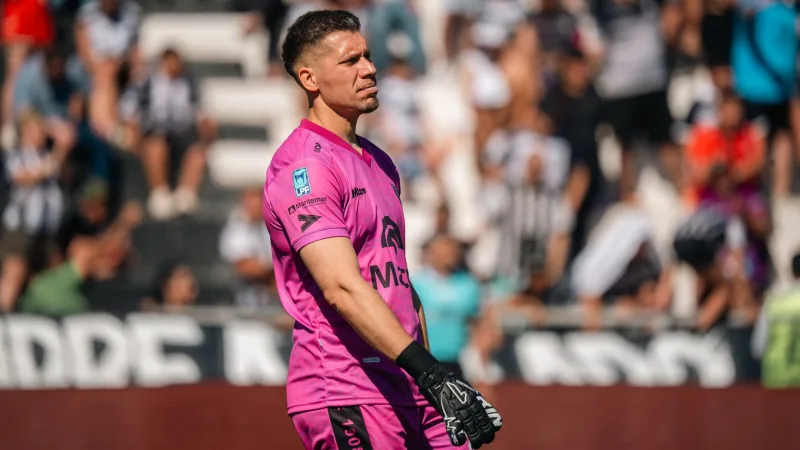 Soccer goalkeeper wearing a pink jersey focused during a lively outdoor match.