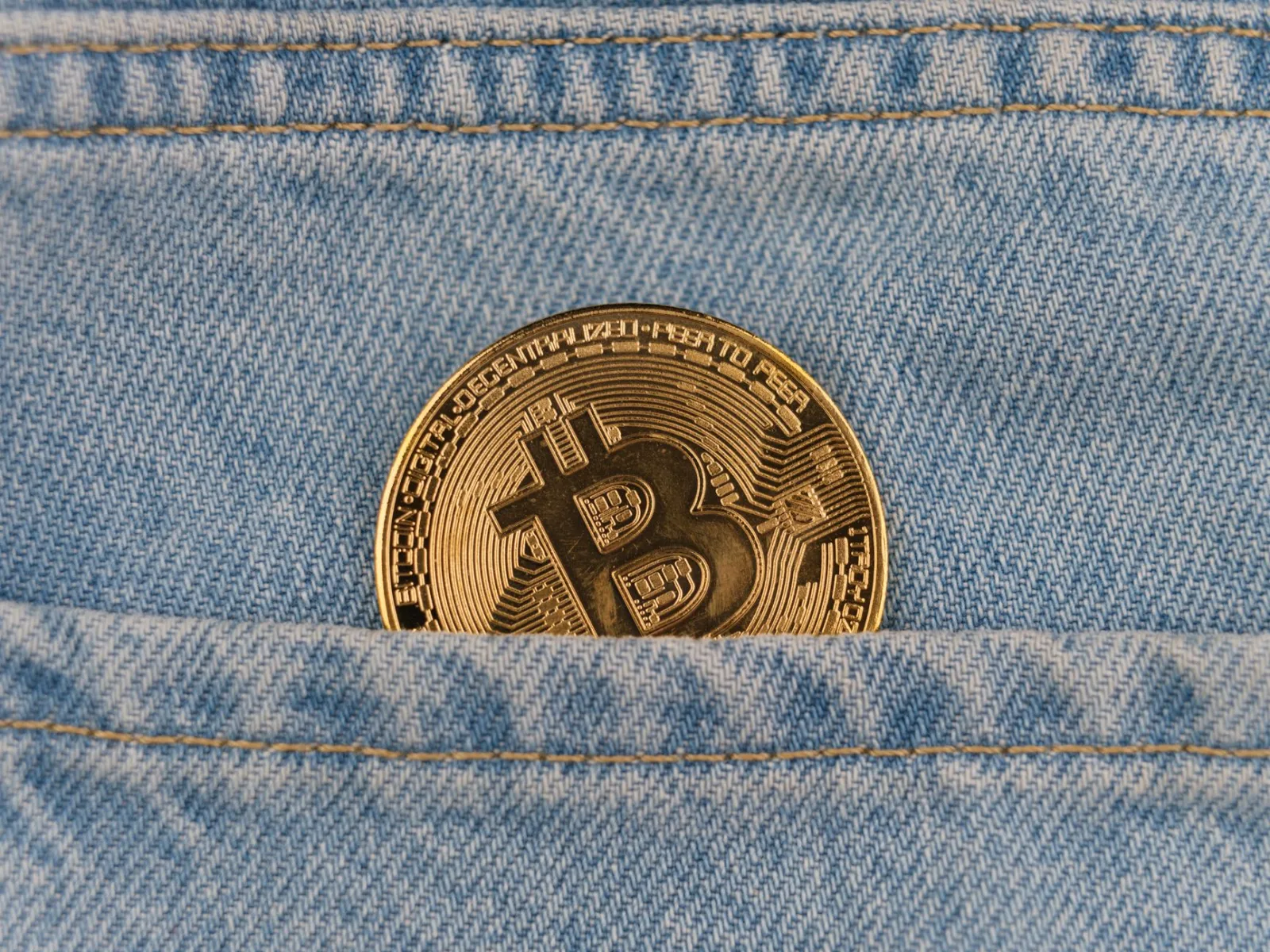 Primer plano de una moneda de bitcoin en un bolsillo de mezclilla, que simboliza las criptomonedas y las finanzas.