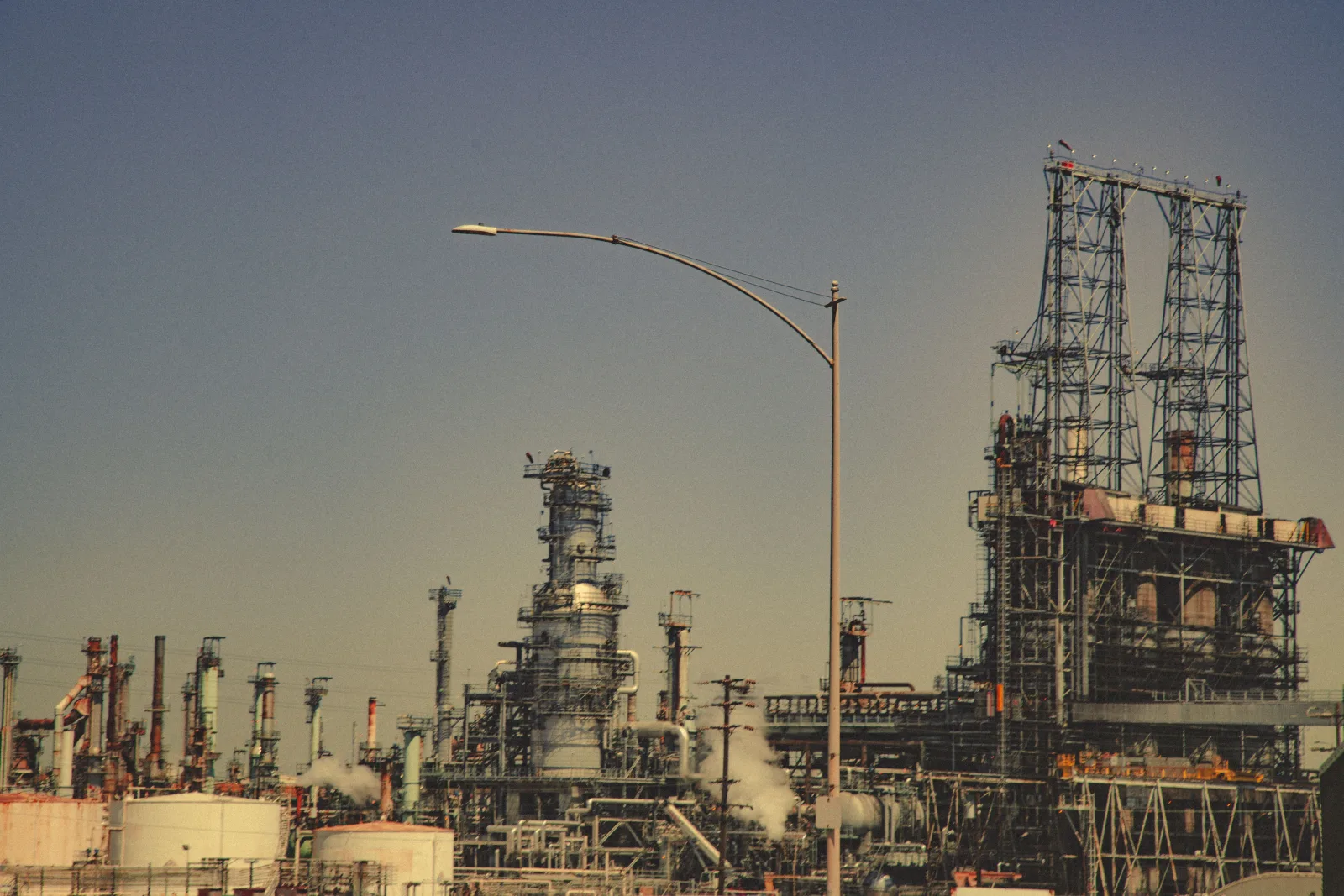 Una gran refinería industrial con tuberías y torres bajo un cielo azul despejado durante el día.