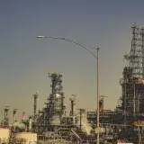 Una gran refinería industrial con tuberías y torres bajo un cielo azul despejado durante el día.