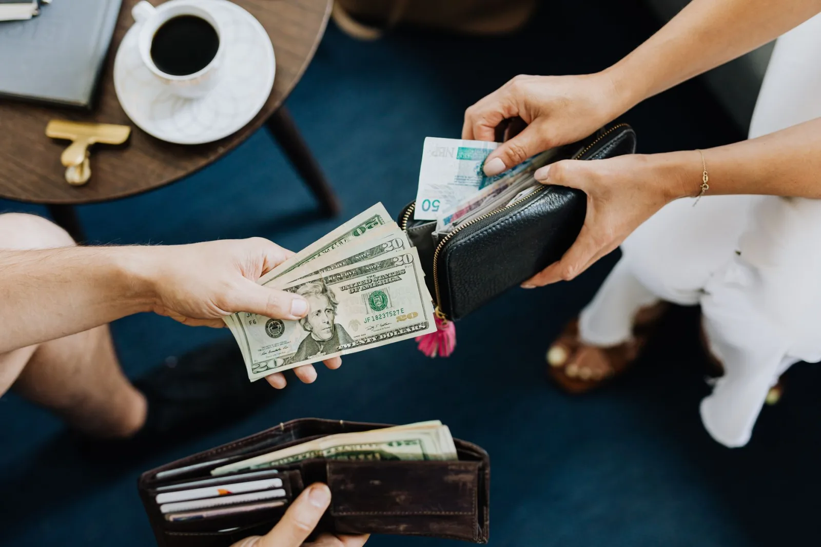 Primer plano de dos personas intercambiando dólares estadounidenses y moneda con carteras sobre una mesa.