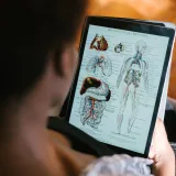 Una mujer estudia diagramas de anatomía en una tableta en el interior, concentrada en el material educativo.