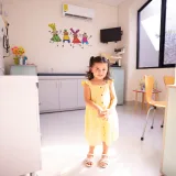 Adorable child smiling in a bright medical clinic, wearing a yellow dress and enjoying a sunny day.