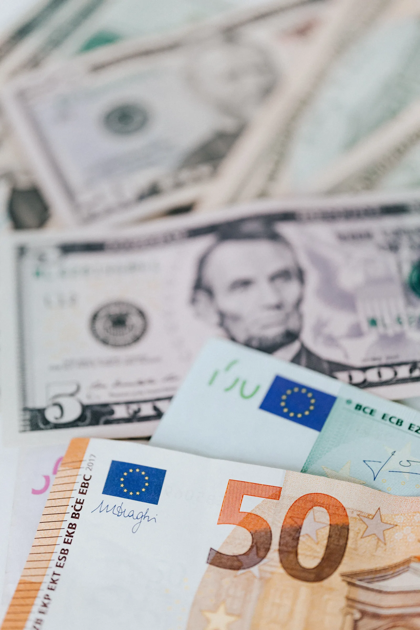 Primer plano de billetes de dólar y euro de distintas denominaciones esparcidos sobre una mesa.