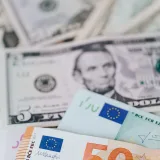 Primer plano de billetes de dólar y euro de distintas denominaciones esparcidos sobre una mesa.