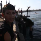 A boy sits by the water as children play, creating a lively scene in Gaza's coastal area.