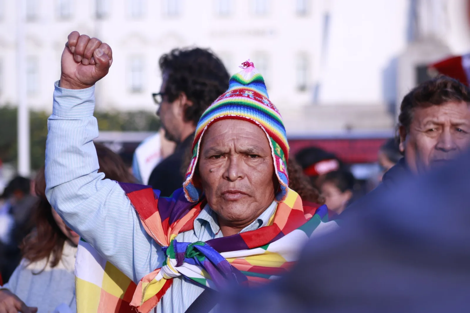 Un hombre mayor con vestimenta colorida levanta el puño durante un encuentro cultural en Perú.
