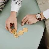 Close-up of hands holding bitcoin coins on a green sofa, emphasizing digital currency trends.