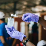 Plano recortado de personas anónimas de diversas etnias mostrando un matraz y una varilla de vidrio con una sustancia química espesa en un laboratorio, con el fondo desenfocado.