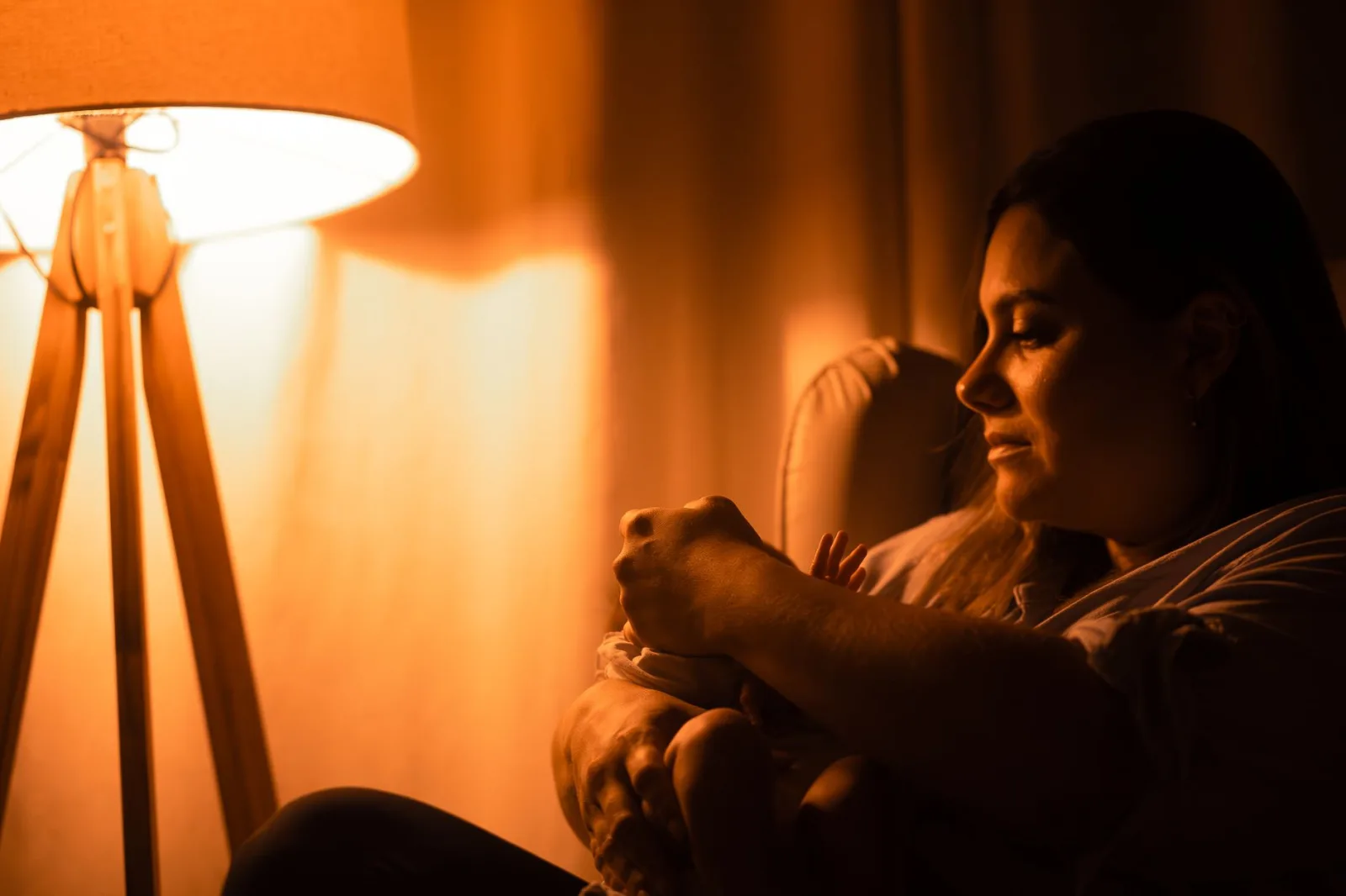 Una madre acuna tiernamente a su bebé bajo la luz cálida y tenue de una lámpara.