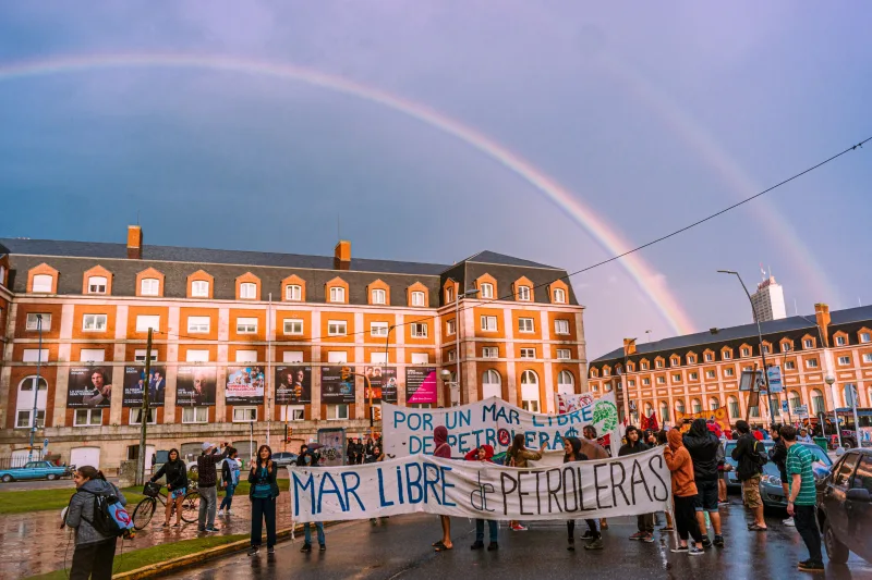 People protesting against oil exploration in Mar del Plata, Argentina under a striking double rainbow.
