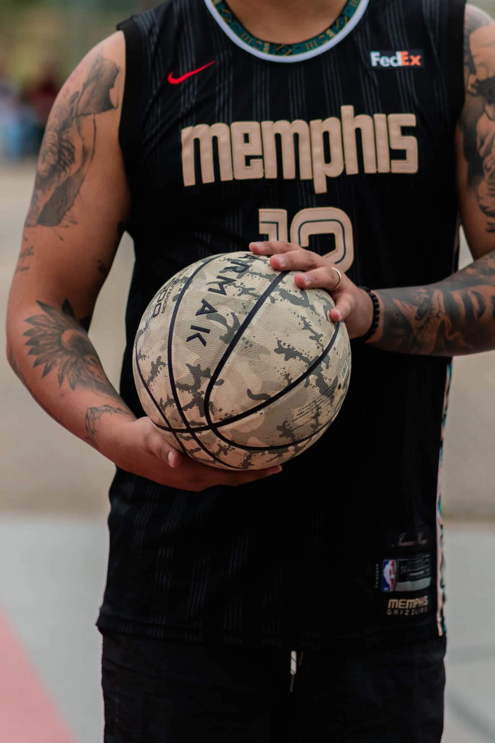Primer plano de un atleta tatuado sosteniendo un balón de baloncesto gastado y vistiendo una camiseta de Memphis.