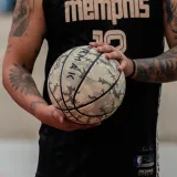Primer plano de un atleta tatuado sosteniendo un balón de baloncesto gastado y vistiendo una camiseta de Memphis.