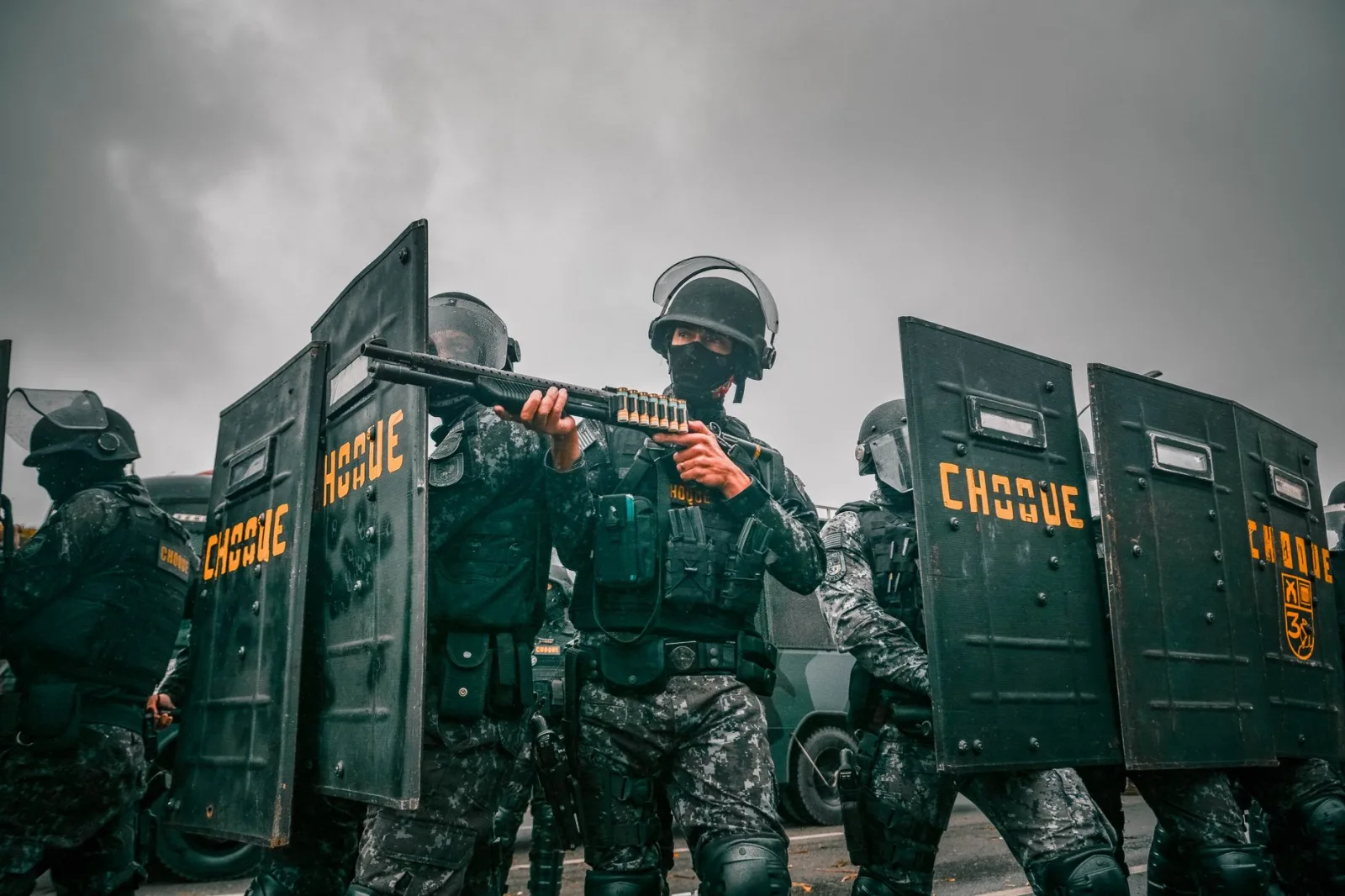 Agentes antidisturbios con equipo de camuflaje y escudos durante un operativo en un día nublado.
