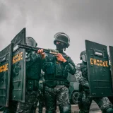 Agentes antidisturbios con equipo de camuflaje y escudos durante un operativo en un día nublado.