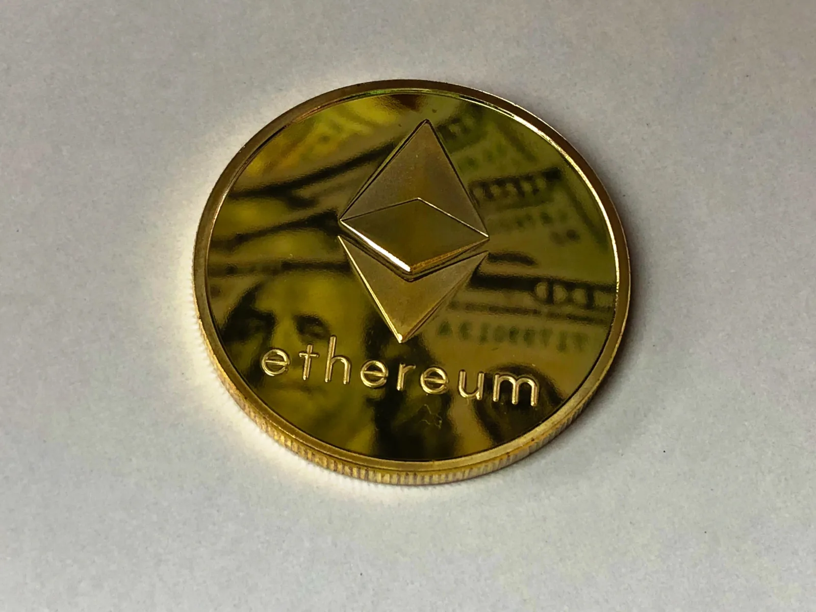 Primer plano de una moneda de Ethereum brillante que refleja un billete de dólar, simbolizando la moneda digital y la riqueza.